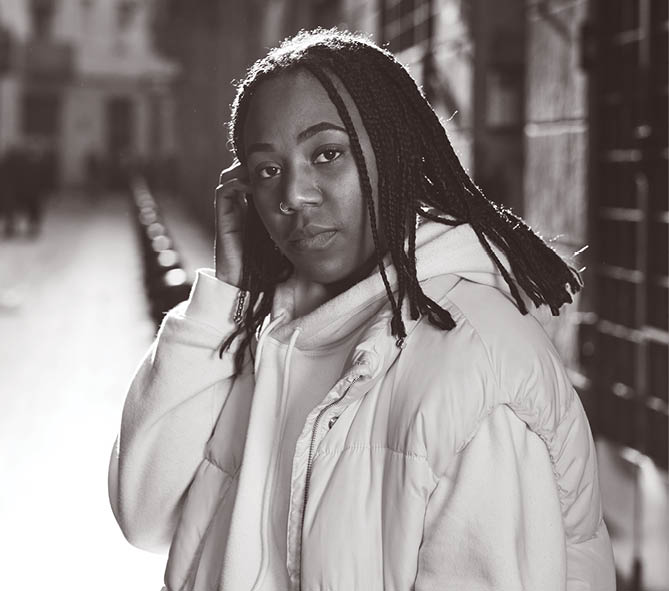 Portrait of young african american woman looking to the camera with serious face while standing outdoors on the street. Urban concept.